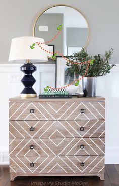 a dresser with a mirror and lamp on top of it in front of a white wall