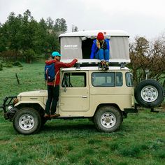 two people standing on top of an off - road vehicle in the middle of a field