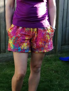 a woman standing in the grass wearing colorful shorts