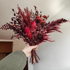 a person holding a bunch of flowers in their hand with red foliage on the stems