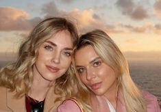 two beautiful young women standing next to each other near the ocean in front of a cloudy sky