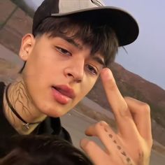 a young man making the peace sign with his hand while wearing a baseball cap and black shirt