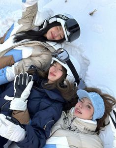 three young women laying in the snow wearing skis and holding onto each other's arms