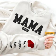 a person holding onto a white sweatshirt with the word maa on it and two red hearts