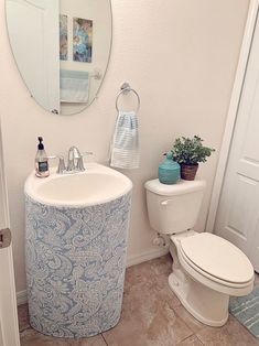 a white toilet sitting next to a sink in a bathroom under a mirror and a potted plant