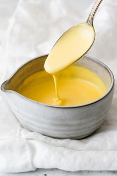 a spoon full of yellow liquid being poured into a bowl with white cloth on the side