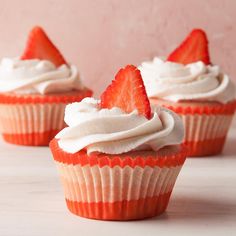 three cupcakes with white frosting and strawberries on top are sitting next to each other