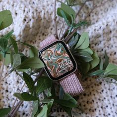 an apple watch sitting on top of a pink wristband next to some green leaves