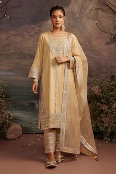 Honey gold kurta with gota patti trims and bead embroidery. Comes with straight pants and dupatta.
Component: 3
Pattern: Embroidery
Type Of Work: Gota Patti
Neckline: Round
Sleeve Type: Full
Fabric: Cotton Silk and Organza
Color: Gold
Other Details: 
Beaded tassels in front
Side slits
Dupatta with embroidered border and tassels at the ends
Occasion: Puja - Aza Fashions Traditional Gold Palazzo Set With Zari Work, Gold Palazzo Set For Eid With Traditional Drape, Gold Palazzo Set With Traditional Drape For Eid, Gold Semi-stitched Palazzo Set For Festive Occasions, Gold Palazzo Set With Dupatta For Eid, Bollywood Style Gold Palazzo Set For Eid, Eid Gold Bollywood Palazzo Set, Bollywood Gold Palazzo Set For Eid, Gold Kurta With Traditional Drape In Chinon