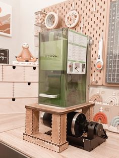 a green machine sitting on top of a wooden table next to a wall mounted clock