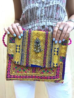 Our new bold embellished clutches come in new statement square shape and are beautiful handmade by local artisans of the Banjara tribe in India. Embellished with bold metallic thread these bags are a stunning accessory to any outfit. All bags are hand-crafted using patchworks of vintage Banjara embroidery and embellishments. According to some authorities, the Banjara lineage goes back some 2000 years. Wear as an over-sized clutch or on your shoulder with the light-weight cotton pompom chain.  Be Multicolor Embroidered Rectangular Clutch For Festivals, Rectangular Multicolor Embroidered Clutch For Festivals, Rectangular Clutch With Multicolor Embroidery For Festivals, Embroidered Rectangular Clutch For Festivals, Multicolor Embroidered Festival Clutch, Traditional Rectangular Clutch For Festivals, Multicolor Rectangular Clutch With Handwork, Bohemian Pouch Clutch For Festive Occasions, Rectangular Multicolor Clutch With Handwork