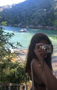 a woman taking a photo with her camera in front of a body of water and mountains