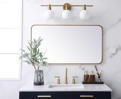 a bathroom vanity with marble counter top and gold faucet, white wall mirror above it