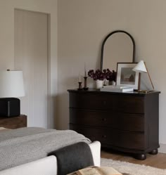 a bed room with a neatly made bed and a mirror on the dresser next to it