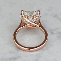 a rose gold engagement ring with a heart cut diamond in the center on a marble surface