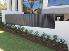 a white house with grass and plants in the front yard, next to a fence