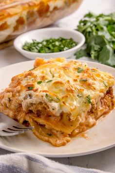 a white plate topped with lasagna covered in cheese and sauce next to greens