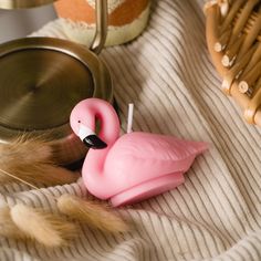 a pink flamingo candle sitting on top of a bed next to a metal bowl