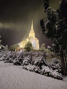 a church lit up at night with snow on the ground and trees in front of it