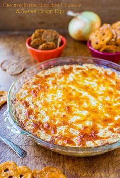 a cheesy dish with crackers, onion rings and other snacks on the table