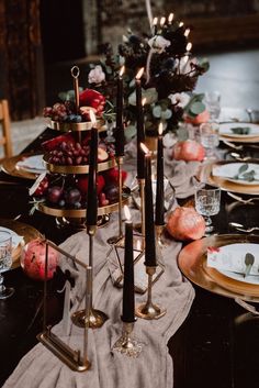 the table is set with candles, plates and fruit on it's trays