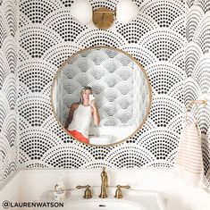 a woman taking a selfie in a mirror above a bathroom sink with black and white wallpaper