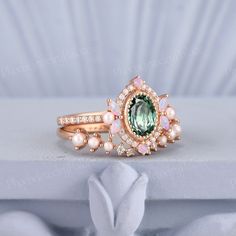 a ring with an oval green stone surrounded by white pearls and pink flowers on top