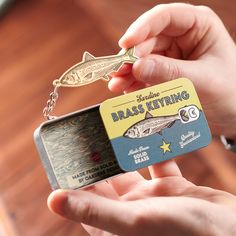 a person holding a small metal keychain with a fish on it