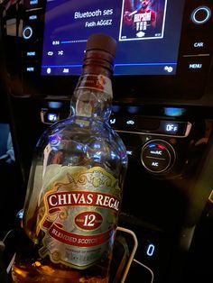 a bottle of chivas recal 12 is sitting in the center console of a car