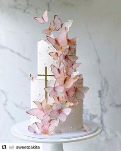 a white cake with pink butterflies on top and a cross in the middle, sitting on a pedestal