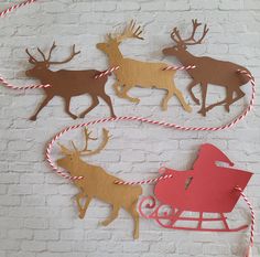 three reindeer sleighs with red and brown paper cutouts hanging on a white brick wall