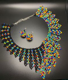 a multicolored beaded necklace and matching earrings on a black surface with a silver chain