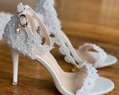 a pair of white high heeled shoes on top of a wooden floor with lace