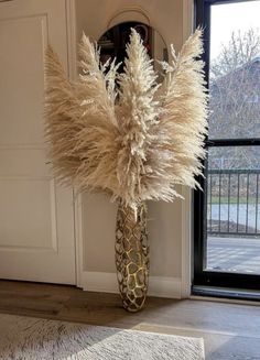 a vase filled with lots of tall dry grass next to a door and window sill