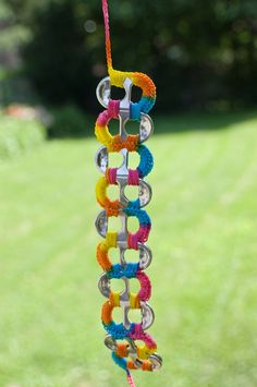 a multicolored wind chime hanging from a string in the grass with trees in the background