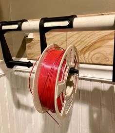 a spool of red wire hanging from a hook on a white wall next to a wooden board