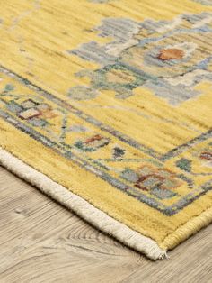 a yellow area rug with an ornate design on the top and bottom, sitting on a wooden floor