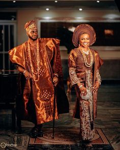 two people dressed in traditional african clothing standing next to each other on a carpeted floor