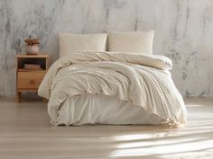 a bed with white sheets and pillows in a bedroom next to a nightstand on a wooden floor