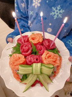 a person holding a plate with flowers and cucumbers on it, lit by candles