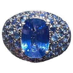 This is an 18K white gold blue sapphires dome cocktail ring. It has an oval cut faceted blue sapphire prong setting in the center, whose measurements are 11.98 x 8.35 x 4.58mm and its weight is approximately 3.78 carat. Pave cluster of fifty one diamond cut sapphires that each one measures 3.0 mm and weights 0.12 carats enhance this queenly ring. It is stamped 750 inside the ring. Blue Cabochon Sapphire Ring In Fine Jewelry Style, Fine Jewelry Blue Cabochon Sapphire Ring, Oval Blue Multi-stone Sapphire Ring, Blue Cabochon Sapphire Ring, Luxury Blue Sapphire Oval Cabochon Ring, Luxury Blue Oval Cabochon Sapphire Ring, Elegant Domed Blue Sapphire Ring, Elegant Blue Domed Sapphire Ring, Blue Sapphire Ring Oval Cabochon