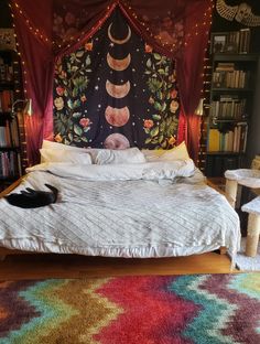 a cat is laying on the bed in front of a colorful wall hanging above it