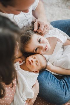 a woman holding a baby while sitting on the floor with other people looking at her