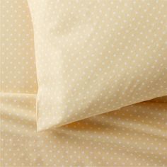 a bed with yellow sheets and white polka dot print on the pillowcase, along with two pillows