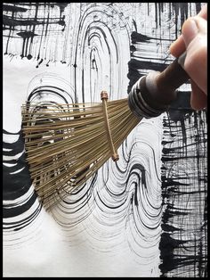 a person is holding a broom over some black and white paint on a piece of paper