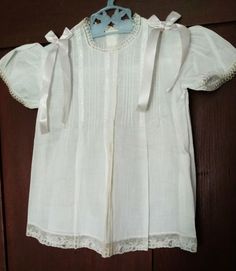 An adorable unworn baby dress from the later 1930s or 1940s. The dress is made in a soft batiste white cotton. The yoke is made of four rows of pin tucks, in a series of four, on the front dress yoke. Each set is separated with a row of feather stitch embroidery.  Narrow lace trim edges the neck line and short puff sleeves.  A wider Alencon lace edges the hem.  Two acetate ribbon bows, with streamers, are attached at the shoulders.  The back of the dress is made on a plain yoke with two buttons fastening the closing. No labels to indicate the origin nor any size tags.  It would probably fit a child about 4 to 6 months of age.  Measurements:  15-1/4" long from the neck line to hem.  9-1/2" across from shoulder to shoulder.  23" around the chest.   Condition:  Unworn and never laundered.  Yo Classic White Vintage Dress With Short Sleeves, Cotton Baptism Dress With Short Sleeves, Classic Short Sleeve Cotton Baptism Dress, Cotton Baptism Dress With Short Sleeves For Daywear, Cotton Short Sleeve Baptism Dress, White Short Sleeve Baptism Dress For Daywear, White Baptism Dress With Short Sleeves For Daywear, White Cotton Vintage Dress With Short Sleeves, Summer Cotton Baptism Dress