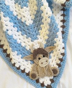 a crocheted blanket with a stuffed animal on it's side and a blue, white, and brown stripe design