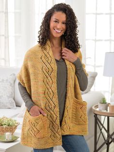 a woman standing in front of a white couch wearing a yellow knitted cardigan