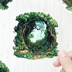 a hand holding up a sticker with an image of a forest in the middle