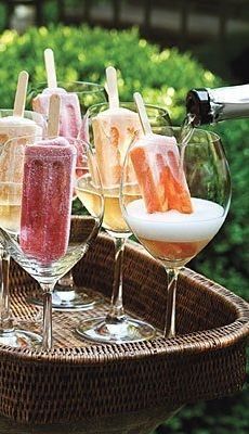 several glasses filled with different types of ice cream on top of a tray in front of bushes